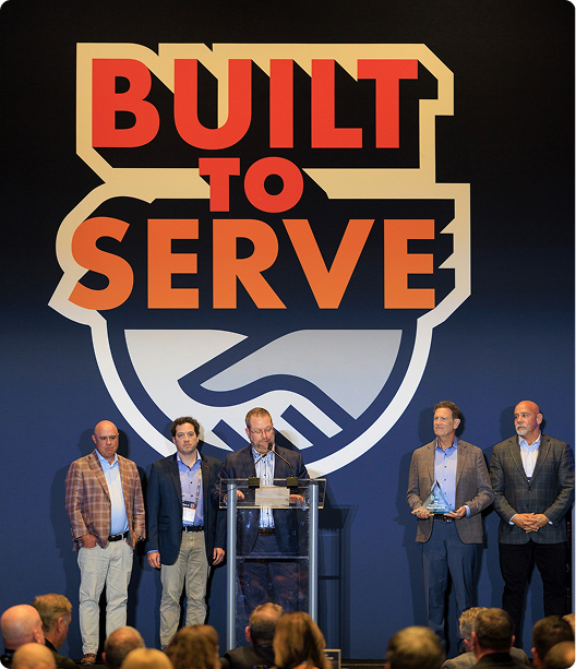 Merit Brass leadership on stage beneath the AD Built to Serve banner during the award acceptance speech
